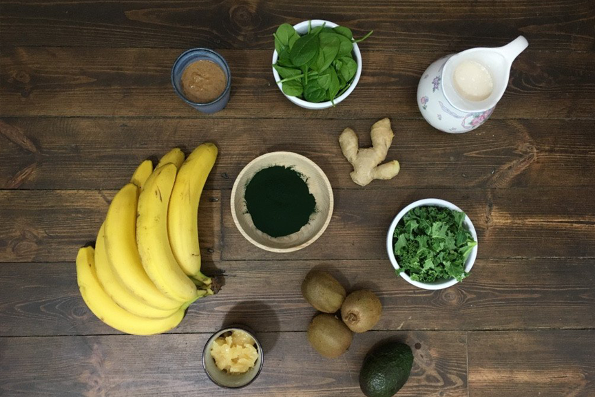 Smoothie ingredients on a table: banana, Spirulina powder, kiwis, and avocado