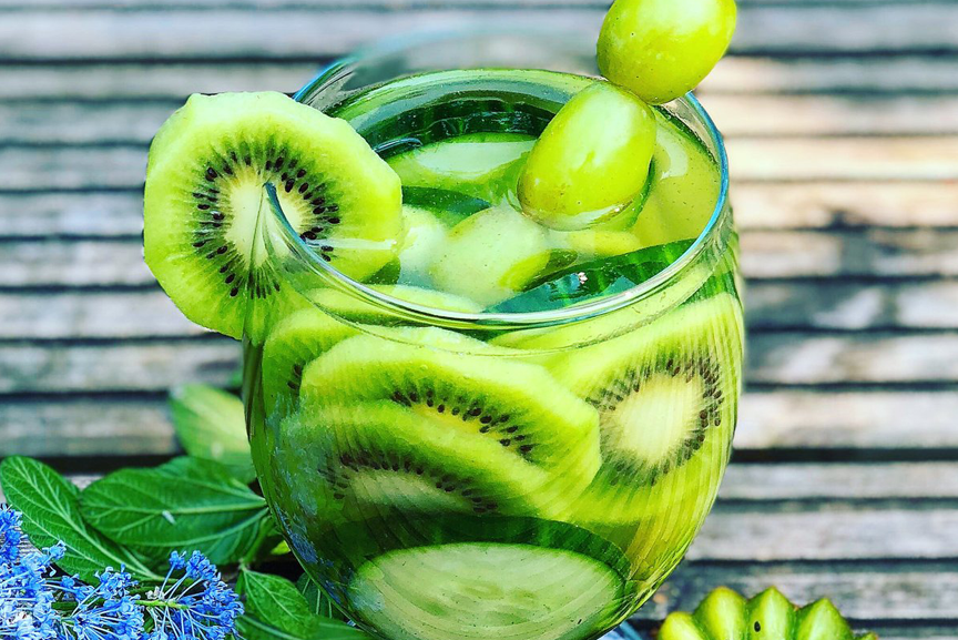 Glass of fruit water stuffed with kiwis and grapes.