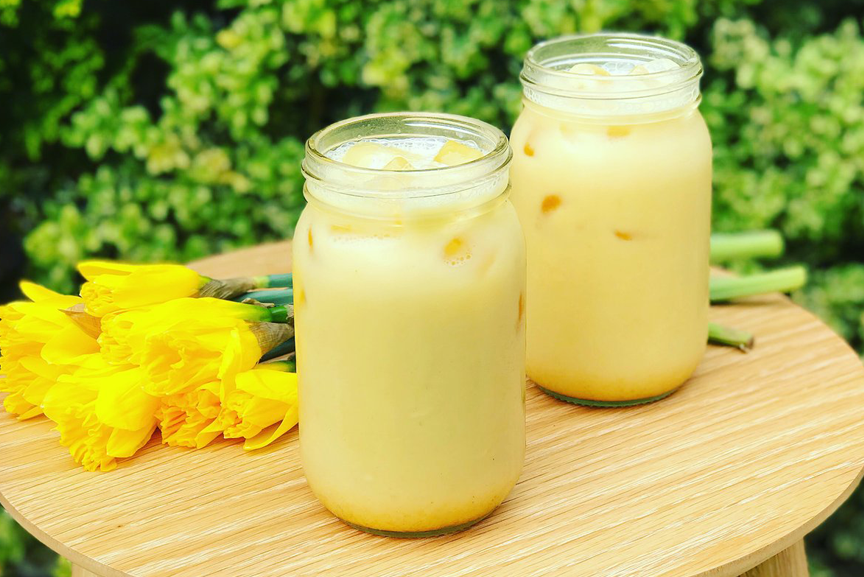 Two jars with iced turmeric latte on a platter with flowers.