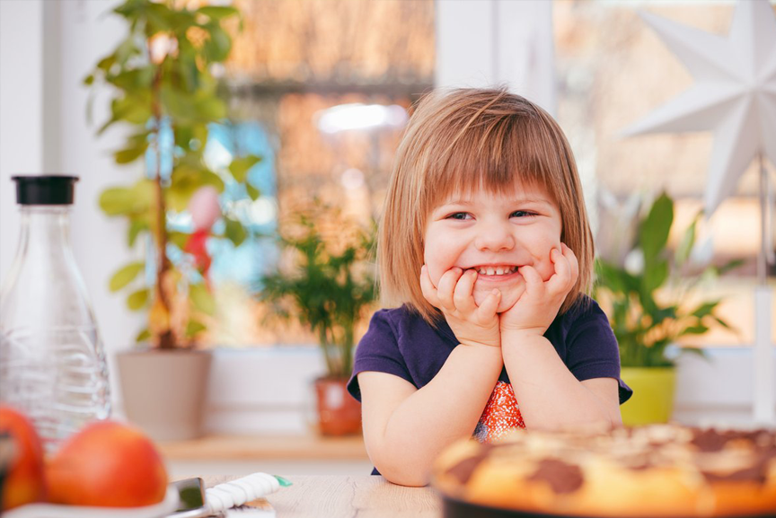 Child smiling and sitting in kitchen.