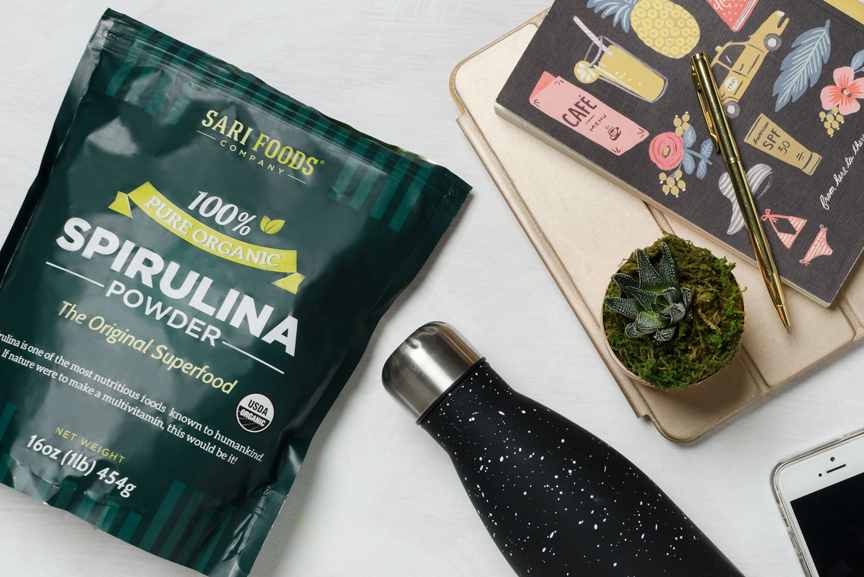 Spirulina package with water bottle and notebooks.