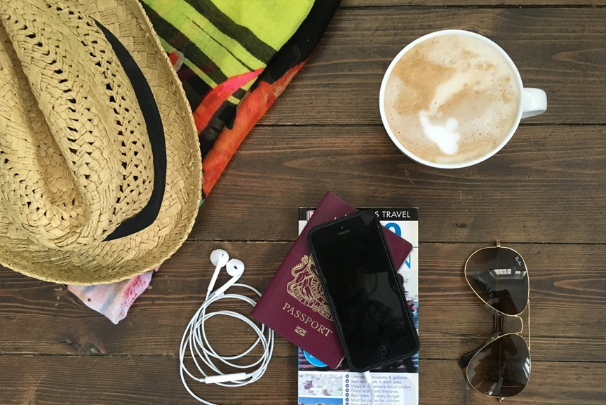 Travel items with a latte and a straw hat